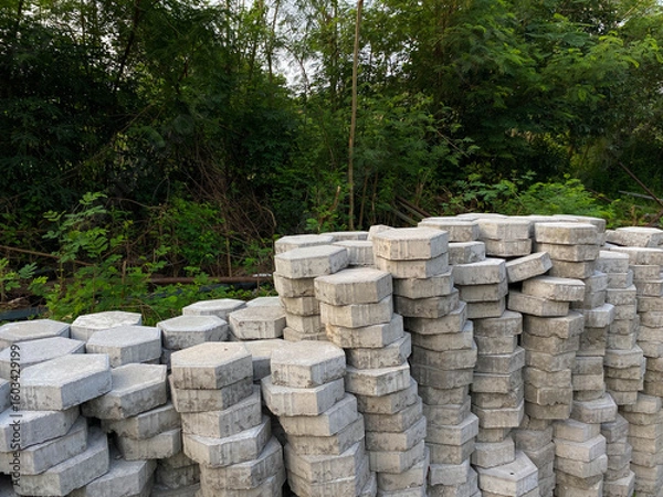 Fototapeta Pile of hexagonal pavers, flooring or concrete block paving, side view, on the edge of green trees