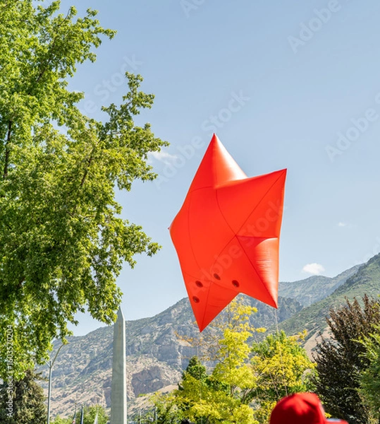 Obraz A large red star-shaped inflatable balloon floats above a crowd during a patriotic outdoor parade