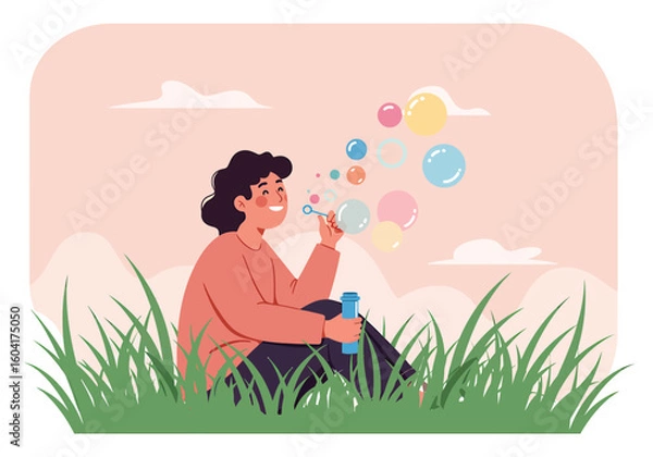 Fototapeta A cheerful young person sits in a grassy field, happily blowing colorful soap bubbles outdoors.