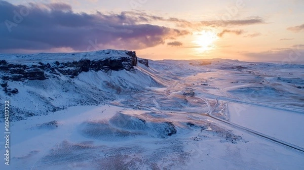Fototapeta A drone photo of the sun setting over a snow-covered Icelandic landscape. 