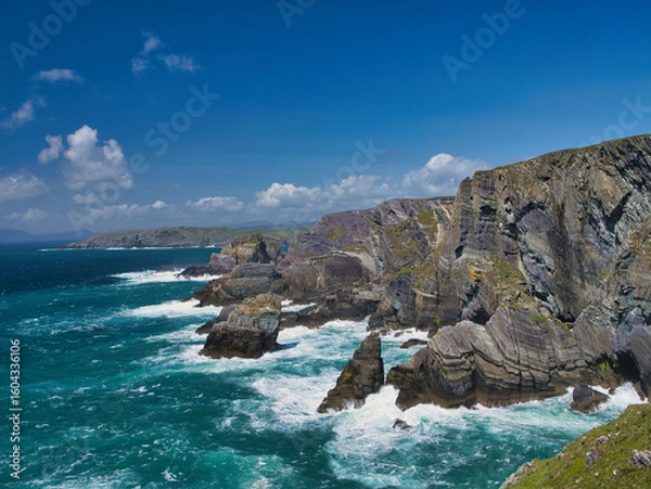 Fototapeta Dramatic cliffs tower over the Atlantic Ocean at Mizen Head, Ireland, under a bright blue sky.