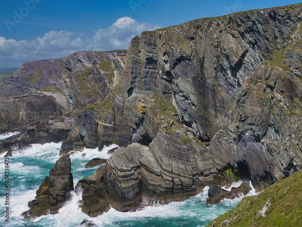 Fototapeta Dramatic cliffs rise against a clear blue sky at Mizen Head, Ireland, with waves crashing below. Captures rugged coastal beauty.