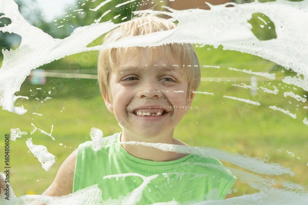 Fototapeta The boy happily looks out the window, which is smeared with soap suds.