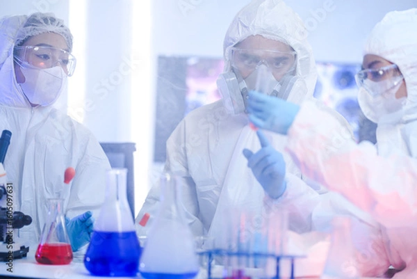 Fototapeta A frontline team of scientists in full protective hazmat suits follows strict protocols in a sterile laboratory. Concept for teamwork, safety, and scientific procedure.