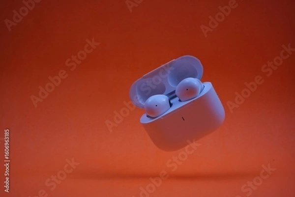 Obraz Modern Wireless Earbuds and Charging Case on Bright Orange Background
