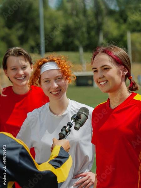 Fototapeta Smiling female football players interviewed after game on sunny day. Concept of representation in media, diversity and sport coverage campaigns.