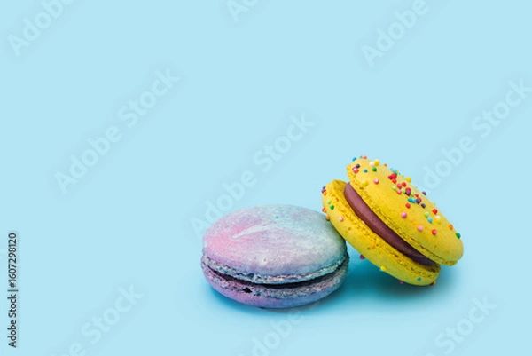 Obraz Sweet colorful macarons isolated on light blue background. Tasty colorful macaroons. Two multi-colored blue and yellow macaroons. French pastry made from egg whites. Culinary and cooking concept.