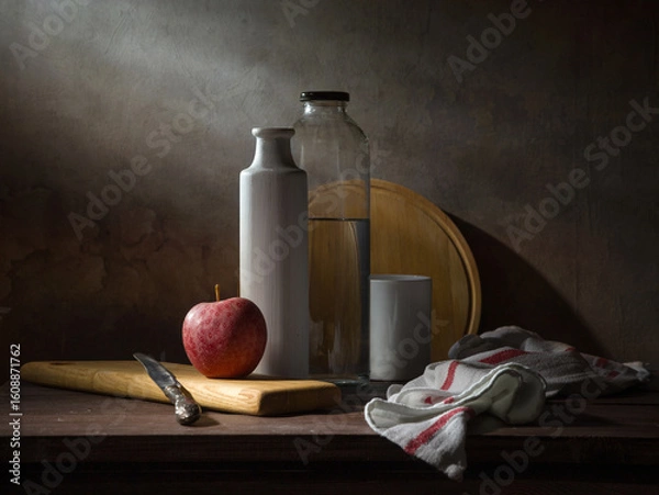 Fototapeta A laconic still life with an apple, a vase, and a bottle of water on a dark background