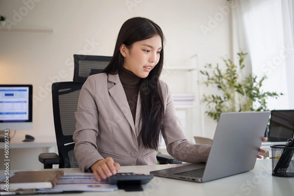 Fototapeta Professional businesswoman using calculator, working on accounting or budgeting tasks in a modern office.