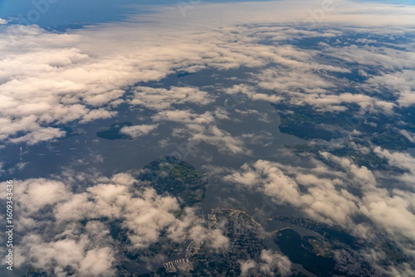Fototapeta Aerial view of land and water through clouds.
