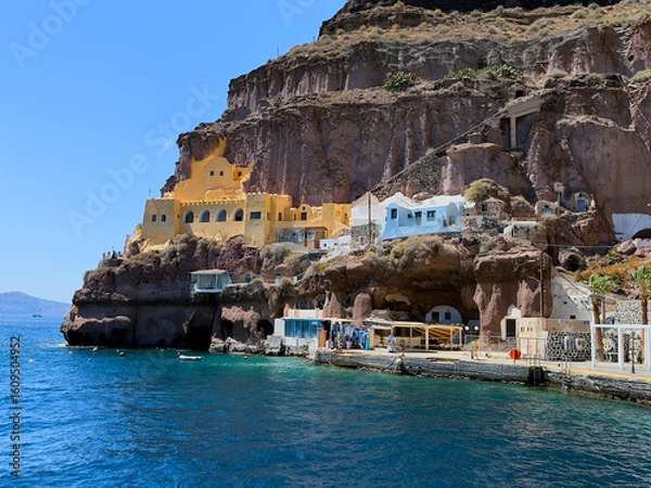 Obraz Vivid yellow and blue houses built into the rocky cliffside above the sea in Santorini, Greece