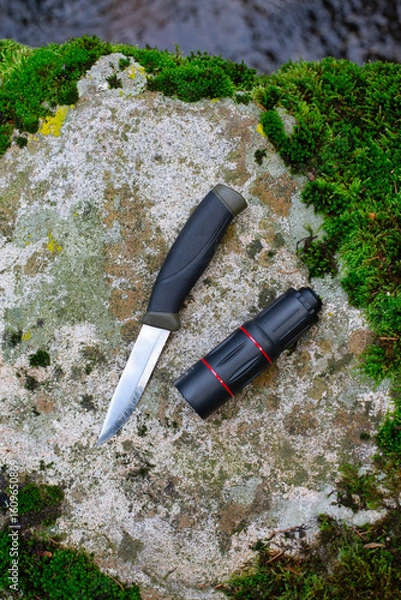 Fototapeta camping knife and monocular on a stone near a river