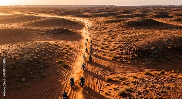 Fototapeta Aerial view of a group of motorcyclists riding on a desert trail during a golden hour sunset creating long shadows and an adventurous atmosphere.