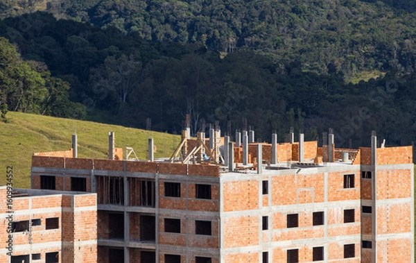 Obraz reinforced concrete and masonry buildings being constructed in front of a large area of preserved forest
