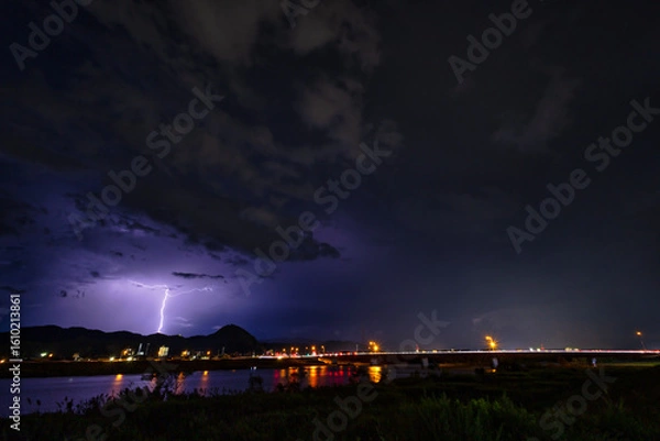 Obraz 河川と街の夜景を背景にした雷雲と稲光の風景