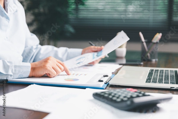 Fototapeta Office businesswoman hand to operate calculator analyzing financial data, counting costs on desk. accounting, financial analysis for business budget planning, calculation support, finance management.