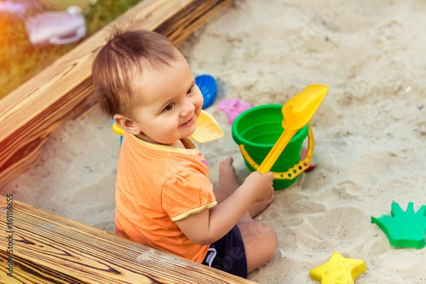 Fototapeta Happy little girl playing in a sandbox on the playground. Summertime children activities