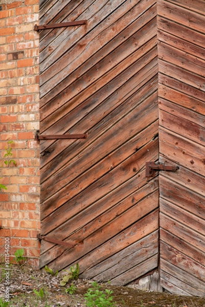 Fototapeta The photo shows a close-up of old wooden gates with diagonal planking set into a brick wall.
