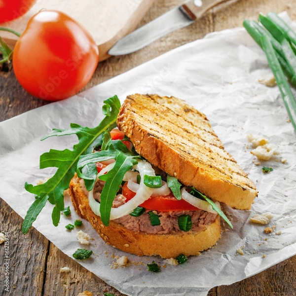 Obraz Classic tuna salad sandwich with tomato, onion and arugula on a table. Delicious healthy meal made of fish, vegetables and toasts.