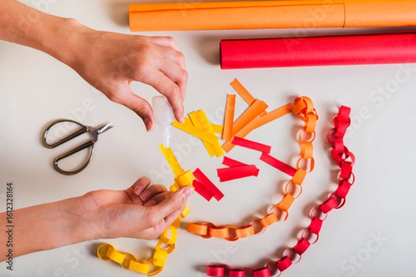 Fototapeta A girl's hands pour glue onto a strip of paper to make a paper chain top view