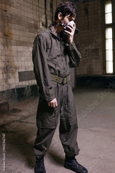 Fototapeta A young man in a military jumpsuit with a protective breathing mask, portrait in a grunge environment