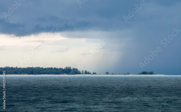 Fototapeta Distant Rain Shower Over Andaman Sea with Coastal Landscape. Dramatic scene over the Andaman Sea shows heavy downpour, contrasting with lighter sky, long stretch of forested coastline under cloudy day