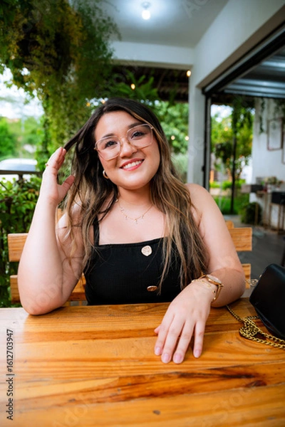 Obraz Young Woman Smiling at Outdoor Café Table with Natural Green Background