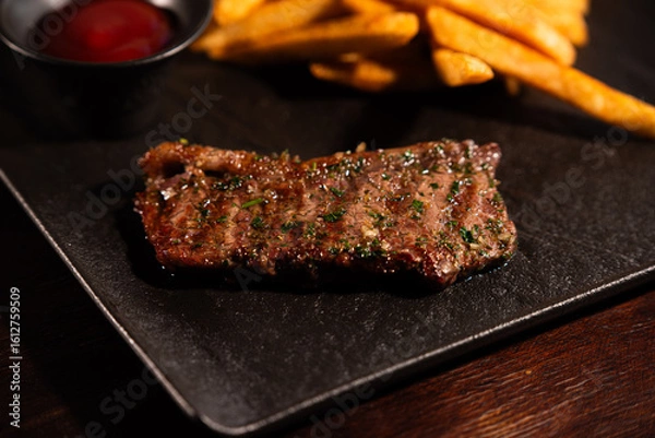 Obraz Grilled Beef Steak with French Fries and Ketchup on Black Plate
