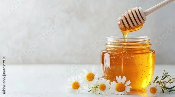 Fototapeta Honey drips from wooden dipper into glass jar, surrounded by chamomile flowers