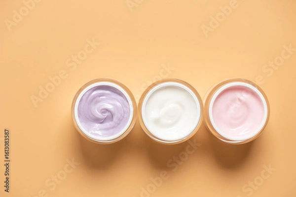 Fototapeta Set of colored cosmetic creams in open jars on pastel yellow background in a row, top view, flat lay,