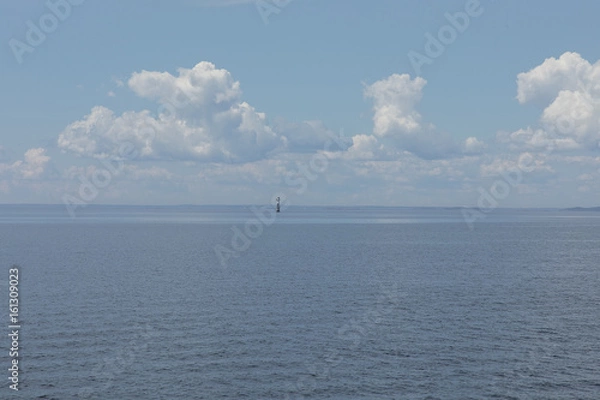 Fototapeta A small lighthouse in the fare end of the sea with some small sailing ships in the background
