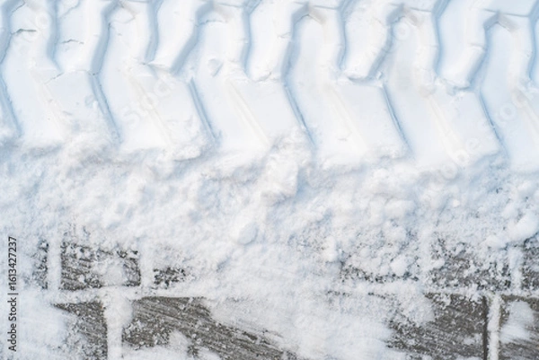 Fototapeta Close-up of tractor tracks on snow-covered cobblestones. Tire tracks on a winter road.