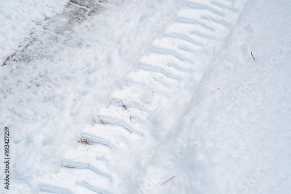 Fototapeta Close-up of tractor tracks on snow-covered cobblestones. Tire tracks on a winter road.