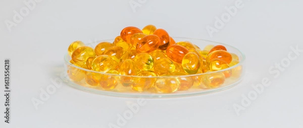 Fototapeta Close-up of yellow gel capsules filled in a transparent glass dish. Conceptual image for omega-3, fish oil, and nutritional health supplements with a clean, minimal medical background.