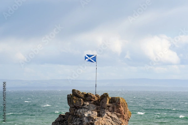 Fototapeta The Scottish flag flying in the wind next to the sea