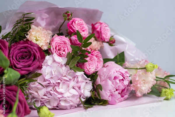 Fototapeta Pink bouquet of roses, peonies, eustoma and hydrangea on a light background. Festive professional flower arrangement in soft pink tissue paper. Romantic bouquet of buds and greenery close-up