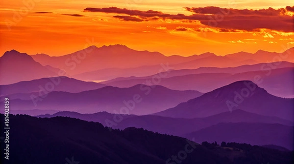 Fototapeta Layers of purple mountains fade into the sunset with an orange sky