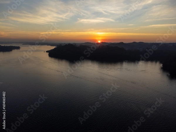 Obraz Orange sun setting between mountains behind large lake