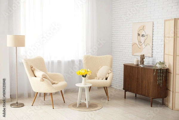 Fototapeta Comfortable armchairs and coffee table with daffodil flowers in interior of living room