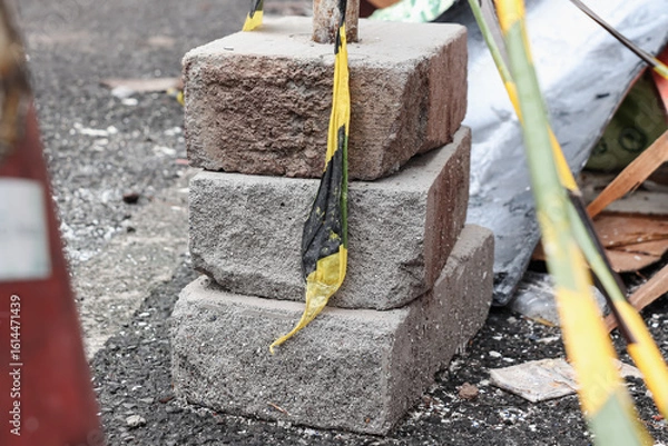 Obraz Three white bricks stacked on the asphalt, a safety line is visible around them and in the background there are the remains of a building