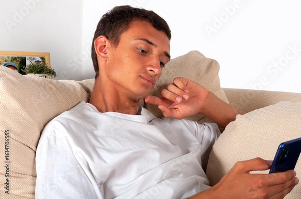 Fototapeta young man with mobile phone lying on sofa at home