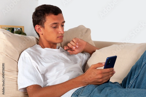 Fototapeta young man with mobile phone lying on sofa at home