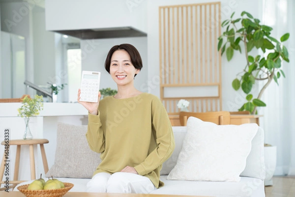 Fototapeta リビングで電卓を持つミドルの女性