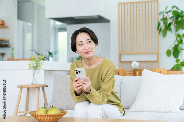 Fototapeta リビングでスマホを見るミドルの女性