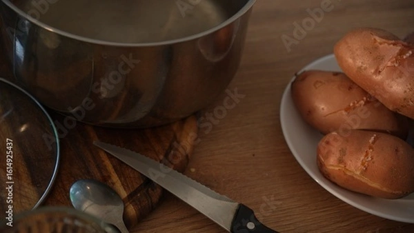 Fototapeta Dolly shot of cooked unpeeled potatoes with pot and knife on table