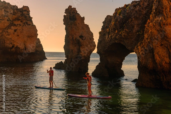 Fototapeta Magnificent view of Ponta da Piedade with two stand-up paddlers at sunrise in Lagos