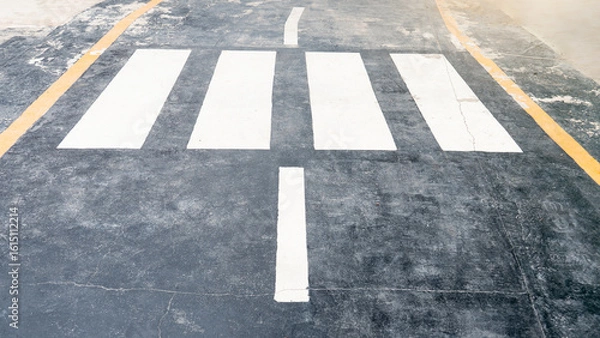 Fototapeta Classic white crosswalk lines on black asphalt with a clear central marker and subtle yellow border. Essential for urban safety or transportation visuals.