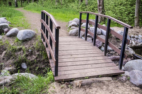 Obraz Trail leads to a small wooden bridge over the creek shore is lined with stones, in the summer forest.