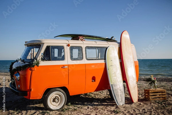 Obraz bus with a surfboard on the roof is a parked near the beach