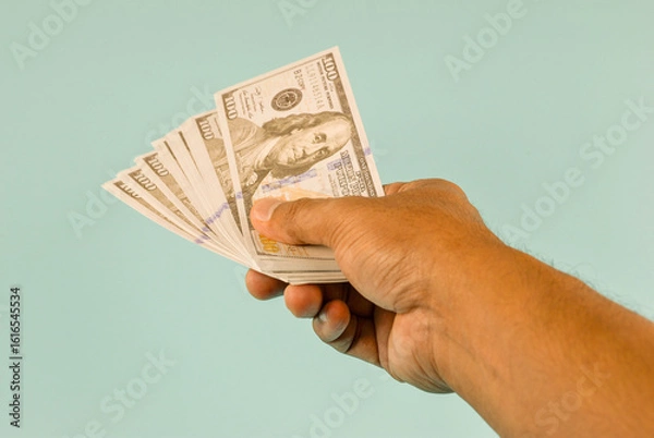 Fototapeta A hand extends, offering a stack of one hundred dollar bills.